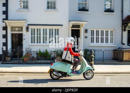 Stilvolle Frau, die einen Motorroller in klassischer Form durch eine Straße in Kensington, London, Großbritannien, fährt. Vespa Primavera 125 Fahrer Stockfoto