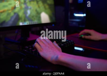 Professionelle Gamer spielen Computer-Videospiel in dunklen Raum, verwenden neonfarbene rgb mechanische Tastatur, Ort für Cybersport-Gaming Stockfoto