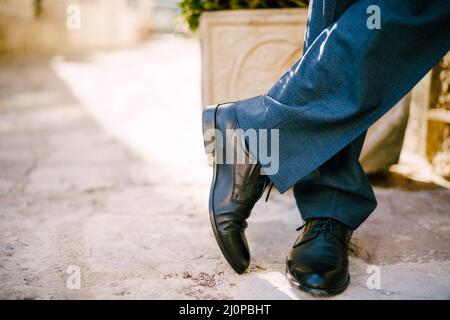 Männliche Füße in schwarzen Schuhen und blauen Hosen auf dem Steinboden. Nahaufnahme Stockfoto