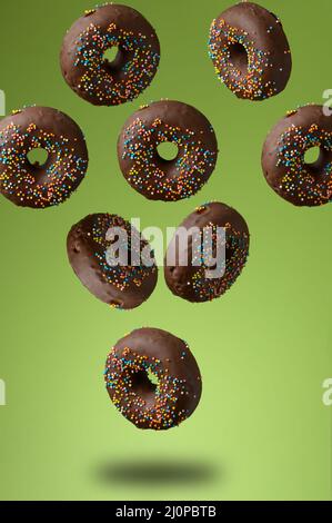 Schokolade runde Donuts mit bunten Zuckerstreuseln schweben auf grünem Hintergrund Stockfoto