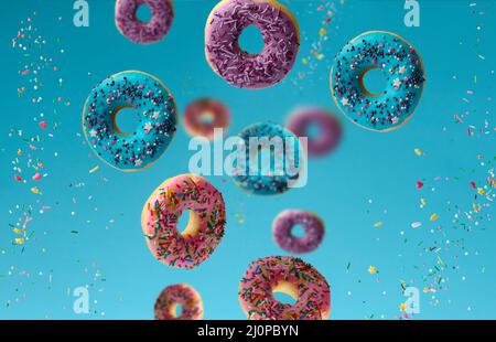 Süße bunte Donuts schweben auf blauem Hintergrund, Zuckerstreuseln fliegen umher Stockfoto