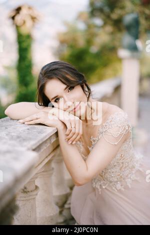 Die Braut sitzt mit dem Kopf auf einer Steinbalustrade. Hochformat Stockfoto