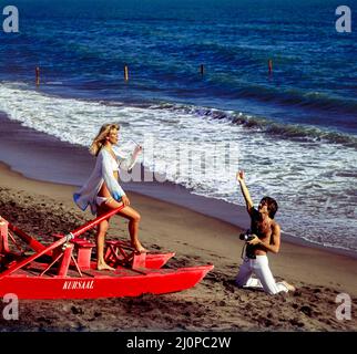 Vintage Italy 1970s, Fotografin fotografiert, Modelemodell weiblich, rotes Ruderrettungsboot, Strand Kursaal, Lido di Ostia, Latium, Europa, Stockfoto