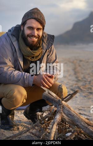 Es wird bald warm. Ein junger Mann, der am Strand ein Feuer baute. Stockfoto