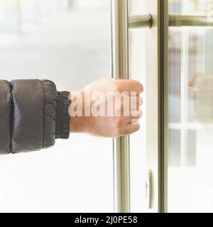 Der Mann nimmt mit der Hand den Türgriff und öffnet die Tür. Ort der Anreicherung von Coronavirus, COVID-19 Stockfoto