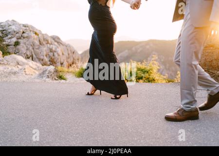 Mann und eine Schwangere gehen auf einer asphaltierten Straße in den Bergen. Nahaufnahme Stockfoto