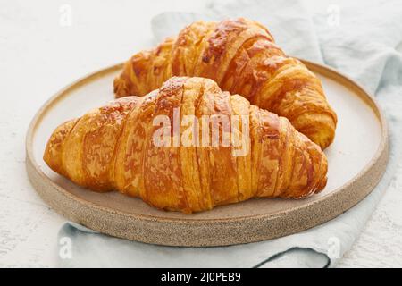 Zwei köstliche Croissants auf dem Teller und ein warmes Getränk im Becher. Morgens französisches Frühstück Stockfoto