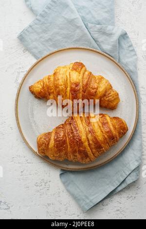 Zwei köstliche Croissants auf dem Teller und ein warmes Getränk im Becher. Morgens französisches Frühstück Stockfoto