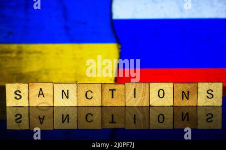 Holzbriefe mit dem Text SANKTIONEN auf dem Hintergrund ukrainische und russische Flagge, das Konzept zum Thema Sanktionen in Russland Stockfoto