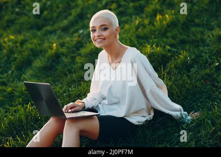 Millenial junge Frau blonde kurze Haare im Freien lächelnd Porträt mit Laptop. Stockfoto