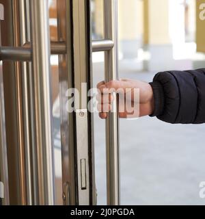 Der Mann nimmt mit der Hand den Türgriff und öffnet die Tür. Ort der Anreicherung von Coronavirus, COVID-19 Stockfoto