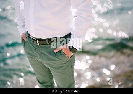 Der Mann in grüner Hose steht mit den Händen in den Taschen über dem glitzernden Wasser. Nahaufnahme Stockfoto