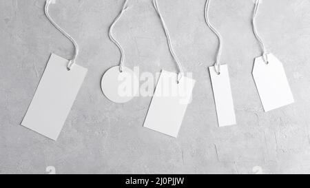 Runder Tag-Mockup, rechteckiger Tag-Mockup, Streifen-Tag-Mockup mit weißer Kordel, Nahaufnahme. Verschiedene Preiskartonetiketten auf grauem Hintergrund. Leere Pap leer Stockfoto