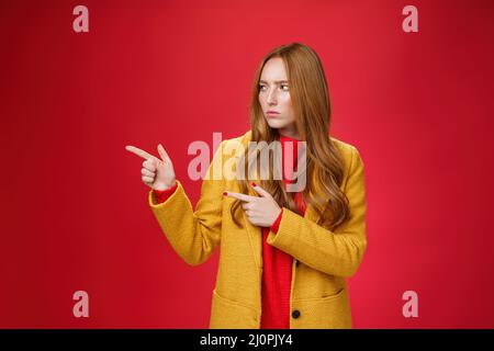 Studioaufnahme einer intensiven, verdächtigen und unzufrieden rothaarigen Hündin in gelbem Fell, die auf eine seriöse linke Quadrierung und Fransen zeigt und aussieht Stockfoto