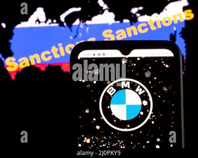 In dieser Abbildung wird das Logo der BMW AG auf einem Smartphone-Bildschirm mit einer russischen Flagge in Form einer Karte des Landes mit der Aufschrift Sanktionen im Hintergrund angezeigt. Stockfoto