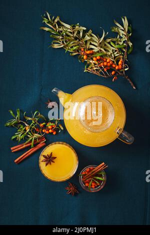 Glas-Teekannen und Glas Sanddorntee mit Zimtstangen und Sternanise auf blauem Hintergrund Stockfoto