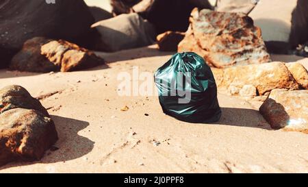 Schwarzer Plastikmüllsack voller Müll am Strand Stockfoto