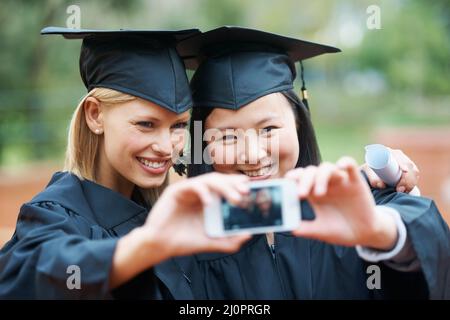 Wir haben schließlich den Abschluss gemacht. Zwei junge Absolventen, die bei der Abschlussfeier ein Selbstporträt machen. Stockfoto