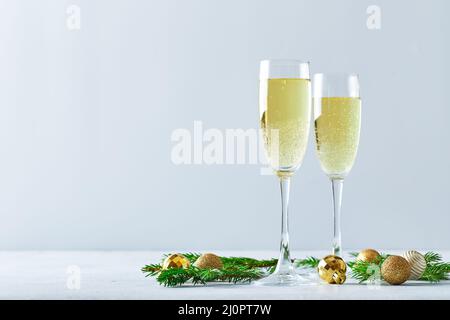 Gläser mit Sekt-Champagner mit Tannenzweigen und goldenen Christbaumdekorationen auf hellem Hintergrund Stockfoto