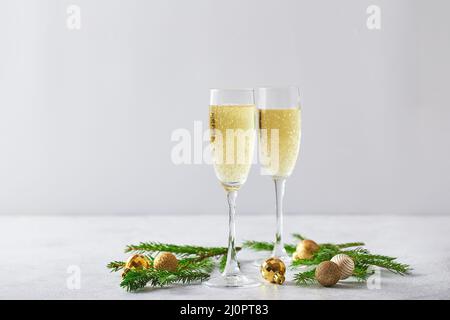 Gläser mit Sekt-Champagner mit Tannenzweigen und goldenen Christbaumdekorationen auf hellem Hintergrund Stockfoto