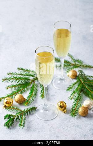 Gläser mit Sekt-Champagner mit Tannenzweigen und goldenen Christbaumdekorationen auf hellem Hintergrund Stockfoto