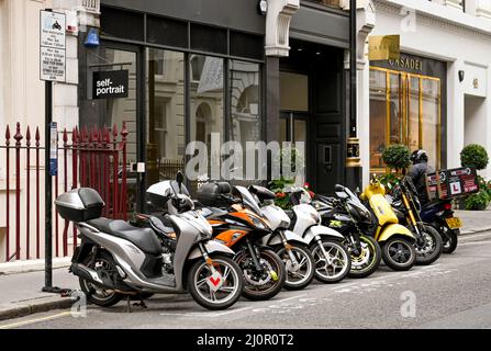 London, England - 2021. August: Eine Reihe von Motorroller, die in einer ausgewiesenen Parkbucht auf einer Londoner Straße geparkt sind Stockfoto