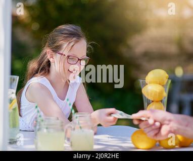 Sie verdienen ihr eigenes Taschengeld, indem Sie ein junger Unternehmer werden. Ein kurzer Schuss eines kleinen Mädchens, das Limonade von ihrem Stand draußen verkauft. Stockfoto