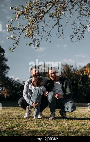 Männlich Gay Paar kümmern sich um ihre kleine Tochter in einem Park. Modernes Familienkonzept. Vertikal. Stockfoto