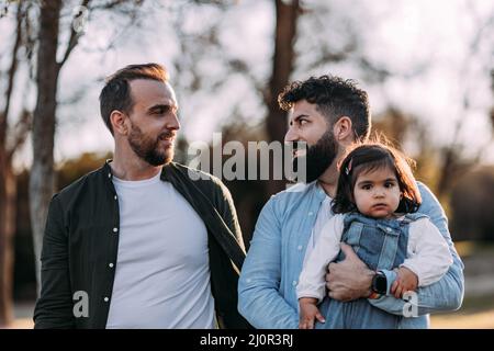 Nahaufnahme eines echten männlichen schwulen Paares, das in den Park geht, verliebt in ihre Tochter in den Armen. Stockfoto