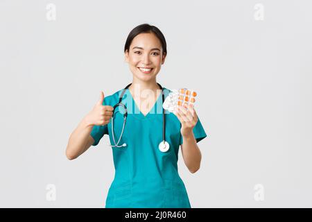 Mitarbeiter im Gesundheitswesen, Virenprävention, Quarantänekampagne Konzept. Selbstbewusst lächelnd asiatische Krankenschwester, Arzt in Scrubs recomm Stockfoto