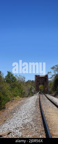 Eisenbahnschienen führen zur Norfork Railroad Bridge in Norfork, Arkansas. Spuren verschwinden in den rostigen Traversen und in den Ozark Wald. Stockfoto