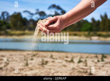 Wir sind auf unserem letzten Stück Wasser. Aufnahme einer nicht erkennbaren Person, die zwei Hände voll Sand hält und zeigt, wie trocken der Bereich draußen ist. Stockfoto