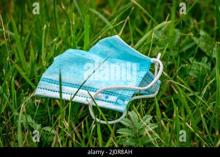 Gesichts-OP-Maske verwendet und auf dem Gras weggeworfen Stockfoto