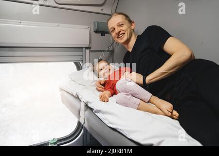 Vater mit Kind travalling in den Zug, Spaß zu genießen Szene durch Fenster, während auf der Eisenbahn zusammen im Schlafwagen fahren Stockfoto