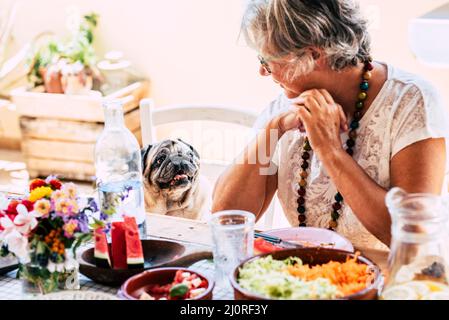 Konzept der Menschen und Tiere Lebensstil, ältere alte Frau schauen mit Liebe ihren lustigen Hund Mops sitzen am Tisch voller Nahrung. Bester Freund zusammen Summen Stockfoto