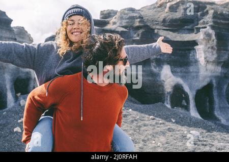 Überglücklich und kostenlos Erwachsene Paar Mann und Frau genießen draußen und malerische Lage. Mann, der eine Frau mit ausgestreckten Armen und einem großen Lächeln im Gesicht trägt. Reisende Stockfoto