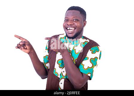 Hübscher, glücklicher junger Mann, der von der Seite mit den Fingern nach innen zeigt und die Kamera anlächelt. Stockfoto