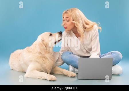 Junge Frau mit pc sitzen auf dem Boden küssen glücklich Hund Stockfoto