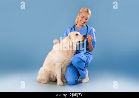 Krankenschwester In Scrubs Uniform Posiert Mit Hund, Der Nahrung Gibt Stockfoto