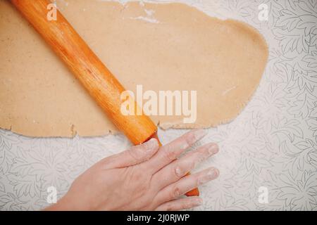 Der Konditor rollt den Teig mit Nudelholz aus und macht leckere Ingwer-Kekse. Dessert kochen und dekorieren Stockfoto