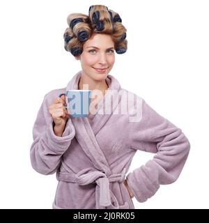 Jeder braucht morgens Hilfe. Studioaufnahme einer Frau mit Lockenwicklern im Haar und einem Bademantel, der Kaffee trinkt. Stockfoto