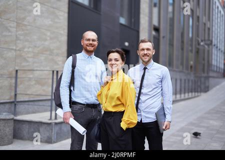 Starke selbstbewusste professionelle Gruppe von Geschäftsleuten, die draußen stehen. Kaukasisches Team aus jungen männlichen und weiblichen Geschäftsführern. Konzept der Finanz-, Immobilien- oder Bauindustrie Stockfoto