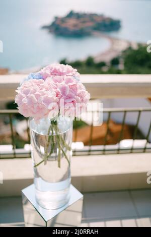 Bouquet von rosa Hortensien steht in einem transparenten hohen Glas auf einem Sockel Stockfoto