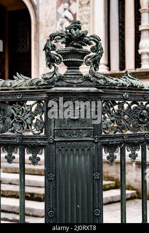 Metallvase mit Blumen auf dem Sockel eines alten schmiedeeisernen Zauns Stockfoto