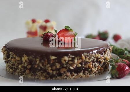 Schokoladenkuchen mit Schokoladenganache und gekrönt mit Walnuss und frischen Erdbeeren. Aufgenommen auf weißem Hintergrund. Stockfoto