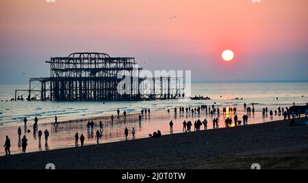 Brighton UK 20. March 2022 - Menschenmassen beobachten den Sonnenuntergang hinter Brighton's West Pier am Frühlings-Tagundnachtgleiche, da sich das warme, sonnige Wetter in ganz Großbritannien in der nächsten Woche fortsetzen wird : Credit Simon Dack / Alamy Live News Stockfoto