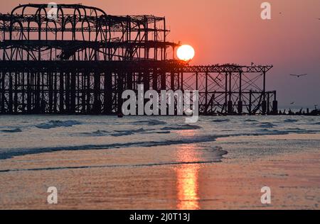 Brighton UK 20. March 2022 - die Sonne untergeht hinter Brighton's West Pier am Frühlings-Tagundnachtgleiche, da sich das warme, sonnige Wetter in ganz Großbritannien in der nächsten Woche fortsetzen wird : Credit Simon Dack / Alamy Live News Stockfoto