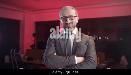 Porträt eines bärtigen Top-Managers mittleren Alters in Büroanzug und Brille. Erfolgreicher glücklicher Geschäftsmann steht, lächelt und schaut in die Kamera Stockfoto