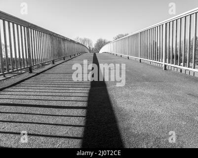 Brücke über einen Fluss, mit dem Geländer als Schatten in der Mitte. In schwarz und weiß Stockfoto