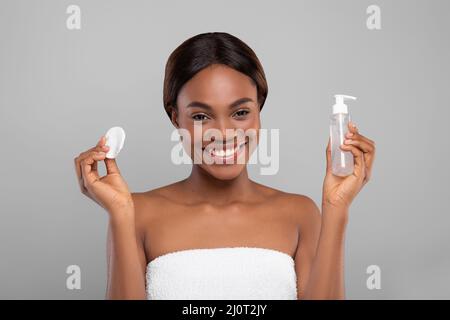 Happy Black Woman Hält Wattepad Und Flasche Mit Gesichtsreinigungsgel Stockfoto